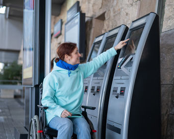 Disabled woman using ticket vending machine outdoors