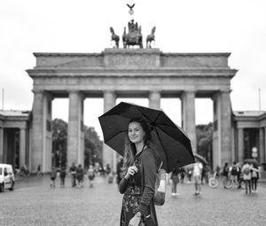 Portrait of smiling woman holding umbrella in front of historical building