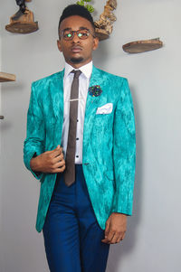 Portrait of young man in suit standing against wall with decoration at home