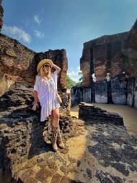 Woman wearing sunglasses and hat standing by old ruin