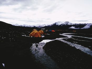 Tent on field by river against cloudy sky