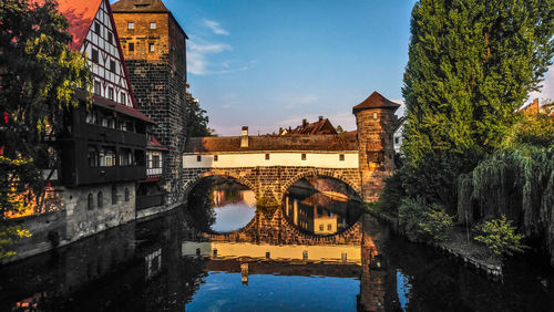 Arch bridge over river by buildings against sky