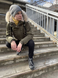 A teenage girl is sitting on the stairs of a bridge in warm clothes 