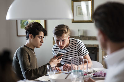 Friend showing phone to teenage boy while sitting at dinner party