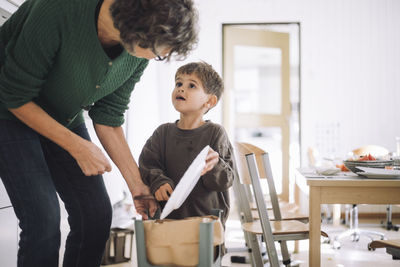 Boy looking at female teacher while throwing food in garbage can at kindergarten