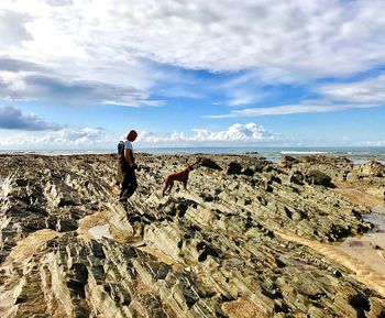 Side view of woman on rock by sea against sky