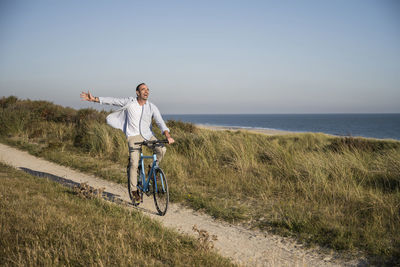 Man riding bicycle on shore against sky