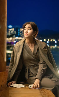 Young woman looking away while sitting on table at night