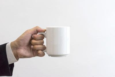 Close-up of hand holding coffee cup against white background