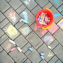 Directly above shot of chalks in container by drawings on footpath