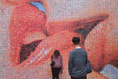 Rear view of people standing against brick wall