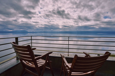 Empty chairs and table against sea against sky