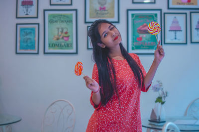 Portrait of young woman holding sweet food against wall