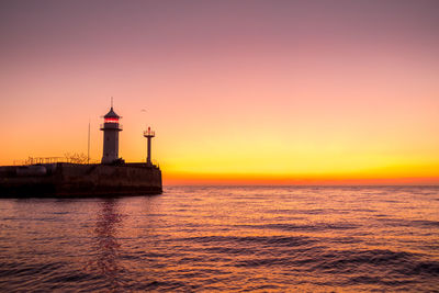 Lighthouse by sea against sky during sunset