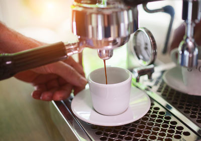 Close-up of person holding cup at espresso maker 