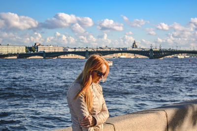 Young woman standing by river against sky in city