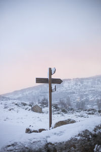 Cross on snow covered land against sky