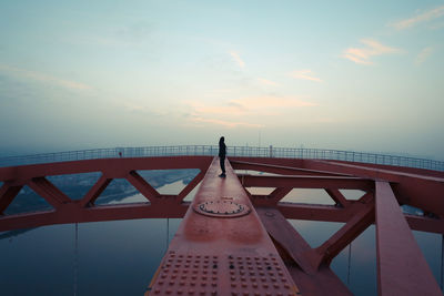 Man standing on railing over river against sky