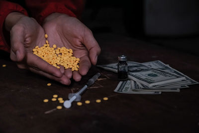 Close-up of hand holding pills with drug and paper currency on table