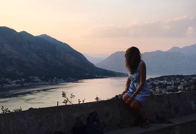 Woman sitting on rock by mountains against sky