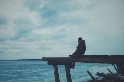 Side view of boy sitting on pier against sea