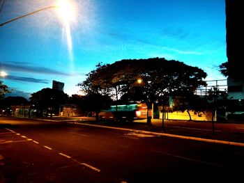Illuminated road by silhouette trees against sky in city