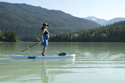 Pregnant woman paddle boarding against mountains