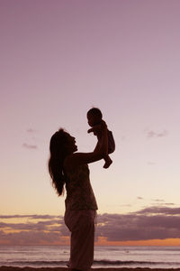 Side view of mother with baby boy on beach during sunset