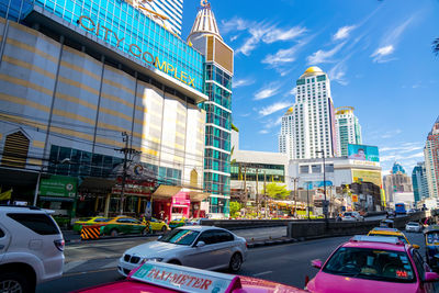 Cars on road by buildings against sky in city