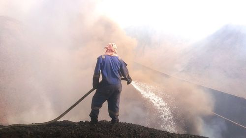 Rear view of a man standing against a burnt coal try to extinguishing it