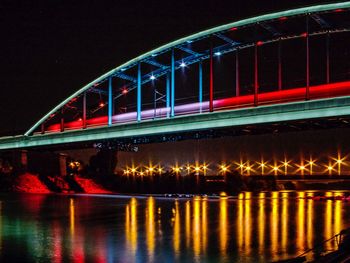 Illuminated bridge over river against sky at night