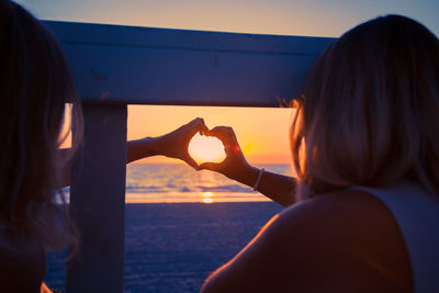 Rear view of woman with arms raised against sky during sunset