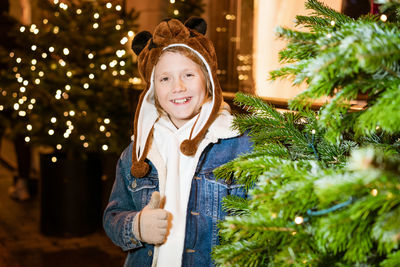 Portrait of smiling young woman standing against illuminated christmas tree