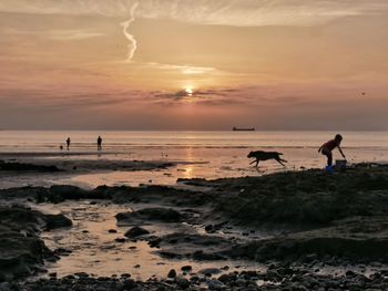 People on beach against sky during sunset