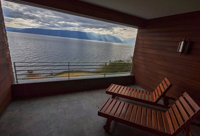 Empty bench by sea against sky seen through window