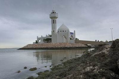 Lighthouse amidst sea and buildings against sky
