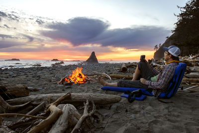 Man sitting by campfire at seashore