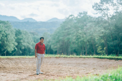 Portrait of man standing on field against trees