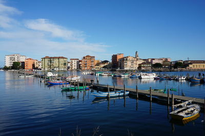 Boats moored in canal by buildings in city against sky