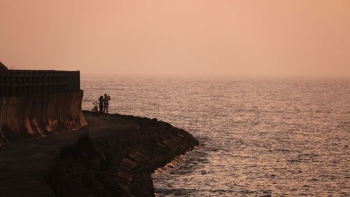 Couple standing by sea against sky during sunset