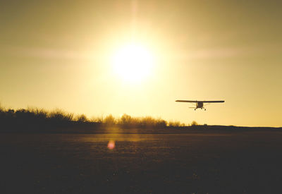 Airplane flying over runway against sky during sunset