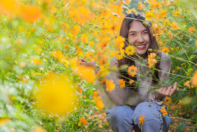 Portrait of smiling woman sitting against yellow flowering plants