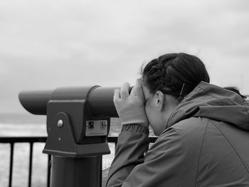 Rear view of a woman using a telescope against sky