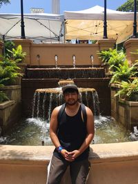 Portrait of man sitting against fountain at park