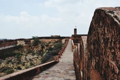 Footpath by wall against sky in city