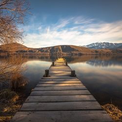 Pier over calm lake by mountains against sky
