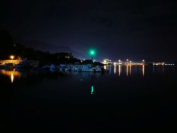 Illuminated city by sea against sky at night