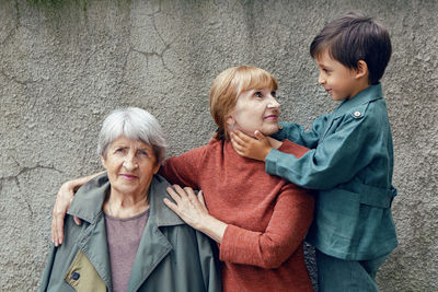 Three generations grandmother great grandmother grandson are standing on the street against a gray 