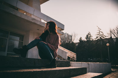 Side view of young woman against built structure