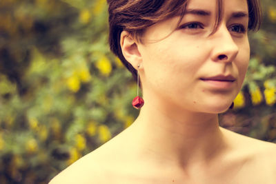 Close-up of young woman wearing red earring against plants